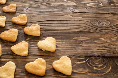 Evde kurabiye pişiren kalpler. Kupa şeklinde kurabiyeler ahşap dokulu bir masanın üzerinde çapraz olarak yatar. Lezzetli çıtır çıtır ve lezzetli kurabiyeler. Mesaj için yer var. Uzayı kopyala Bakım konsepti