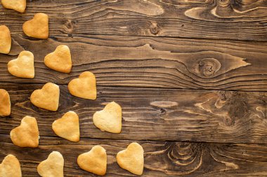 Evde kurabiye pişiren kalpler. Kupa şeklinde kurabiyeler ahşap dokulu bir masanın üzerinde çapraz olarak yatar. Lezzetli çıtır çıtır ve lezzetli kurabiyeler. Mesaj için yer var. Uzayı kopyala Bakım konsepti