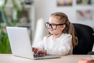 Gözlük takan sevimli küçük kız karantina ve kendini izole etme süresince bilgisayarlı e-öğrenme konseptini kullanıyor. Covid-19 koronavirüs salgınından dolayı uzaktan öğrenim .