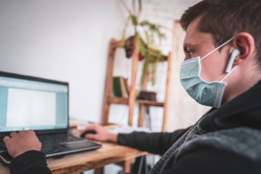 Coronavirus karantinası sırasında dizüstü bilgisayarı olan maskeli aktif bir genç çocuk. Online eğitim kavramı. Sosyal uzaklık, kendini soyutlama. Virüs, grip, salgın COVID-19 kaynaklı uzaktan öğrenme