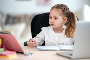 Sevimli küçük bir kız, ödev yapıyor, not defteri yazıyor, karantina ve kendini soyutlama süresince dizüstü bilgisayar kullanıyor, e-öğrenme kavramları kullanıyor. Covid-19 koronavirüs salgınından dolayı uzaktan öğrenim