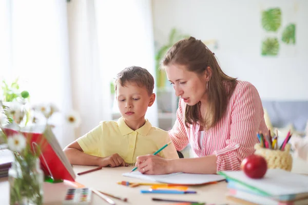 Mother helps son to do lessons. correct the error in home lessons. the tutor is engaged with child, teaches to write and count. out-of-school lessons with a teacher. happy baby in bright room with mom