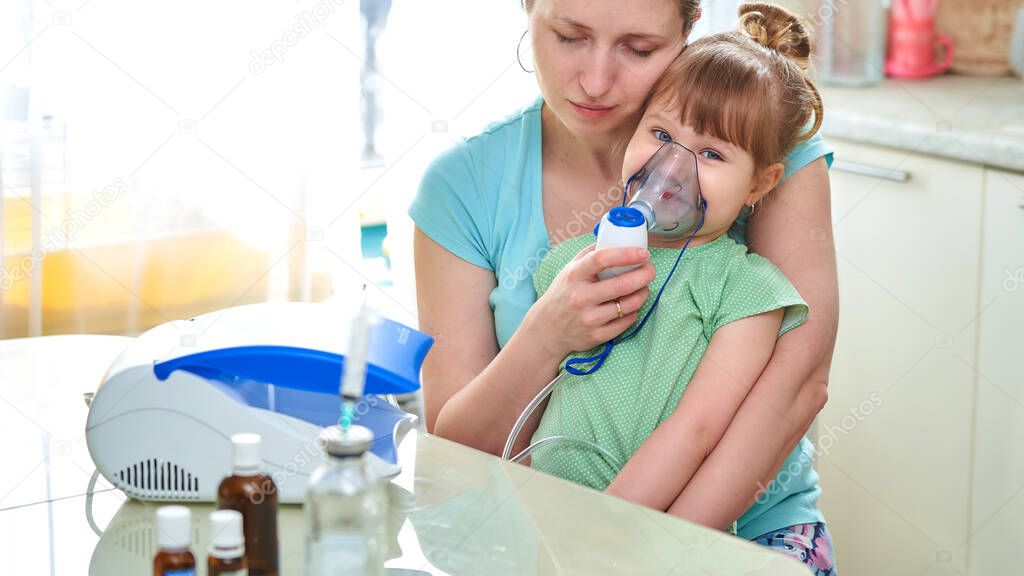 Mother and little girl during inhalation with a nebulizer at home. Cute little baby in the mask of an inhaler. Girl is happy to do inhalation, wants to be healthy. concept of anti-virus and allergies