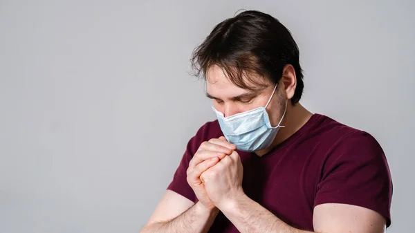 Portrait of a young man in a medical mask, praying for salvation and protection from a dangerous virus. A man wearing a medical protective mask as a preventive measure against COVID-19, SARS, nCov-19