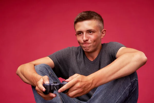 An excited, Tense Man is Playing an Online Computer Game and Competing in video Games Using a Joystick, On a Red Background. Insulation. Leisure Activities At Home. Internet addiction