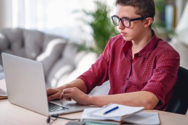 Düşünceli, gözlüklü, ders dinleyen, dizüstü bilgisayar kullanan ve notlar alan genç bir adam. Online öğrenme kavramı. Sosyal uzaklık, kendini izole etme. Uzaklık öğrenimi.