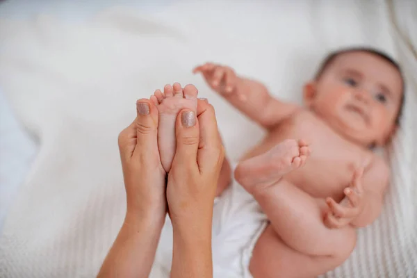 Close-up of children\'s foot massage on the bed. A mother massages the foot of a cute newborn baby\'s foot. Selective focus on the child\'s leg.
