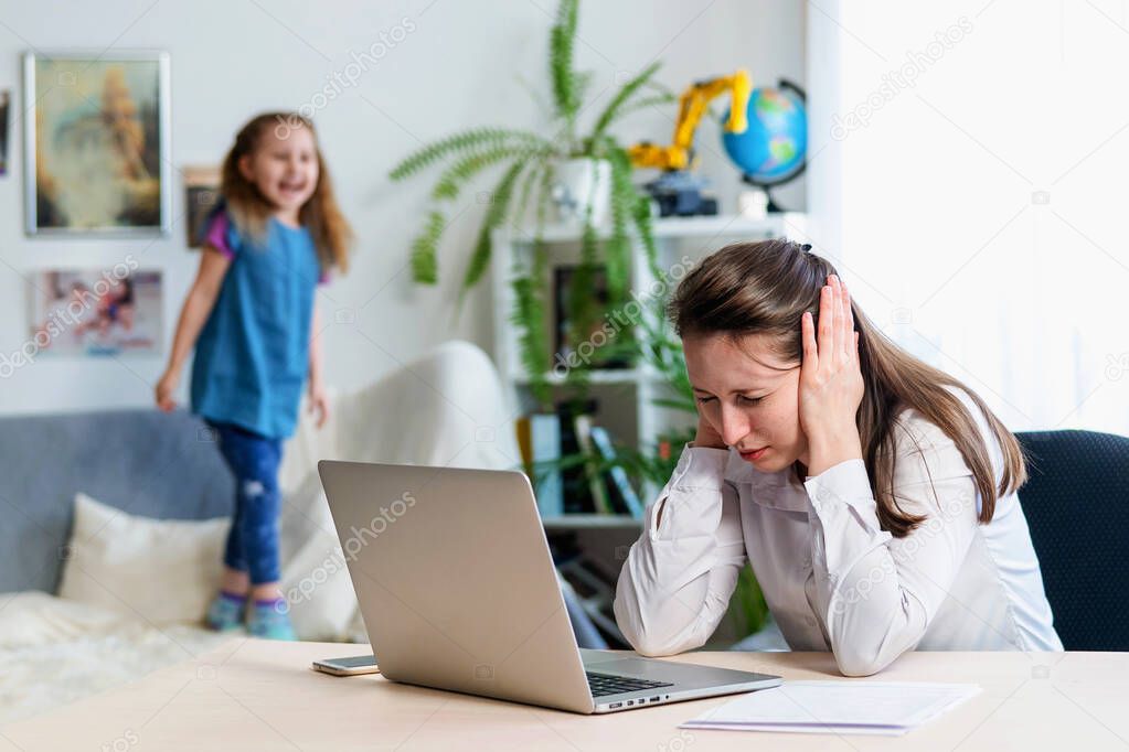 Young mother works at home with laptop, along with a little daughter. Child want to jump, make noise and interfere with work. woman covers her earsSelf-isolation during coronovirus pandemic