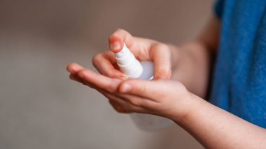 Virüse karşı korumak için maske takan küçük bir çocuk ellerini jel dezenfektanla temizliyor.