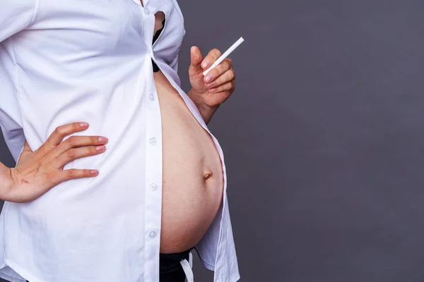 Smoking pregnancy. pregnancy and smoking cigarettes. Harm to the child\'s health . Premature birth. Close up pregnant woman quits smoking.On gray background. Copy space