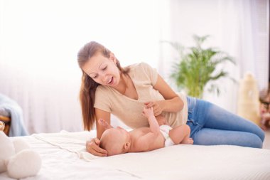 Sevgi dolu bir aile. Genç bir anne küçük bir çocukla birlikte yatakta yatıyor. Kadın gülümsüyor, oynuyor ve bebeğe sarılıyor. Annelik kavramı.