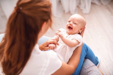 Sevgi dolu bir aile. Genç anne, küçük bir çocukla rahat bir koltukta oturuyor. Kadın gülümser, oynar ve bebeğe sarılır. konsept annelik. Annem yeni doğmuş kızıyla jimnastik yaparak eğleniyor. en üstteki görünüm