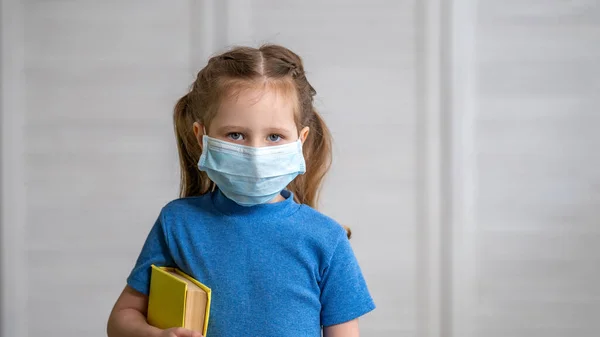 Egy Kislány Orvosi Maszkban Egy Könyvvel Kezében Könnyű Háttérrel Oktatási — Stock Fotó