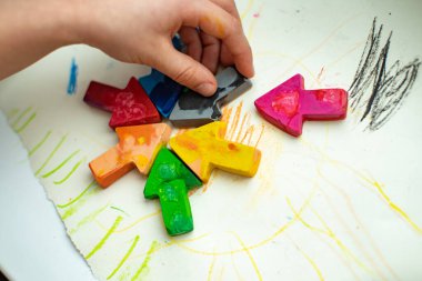 Eski pastel boyaların enkazından ev yapımı balmumu kalemleri yüksek sıcaklıkta silikon şeklinde fırında eriterek yaptım. Ok şeklinde pastel boyalar kağıt üzerinde, çocuk eli kalem tutuyor.