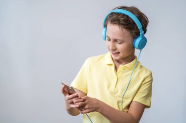 Mutlu çocuk elindeki akıllı telefona bakar, büyük kulaklıklar takar ve müzik dinler. Elinde cep telefonu olan ve film ve video izlemekten zevk alan bir çocuk. Boşluğu kopyala.