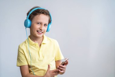 Pozitif çocuk çerçeveye bakar, akıllı telefonu elinde tutar, kulaklık takar ve müzik dinler. Elinde cep telefonu olan ve film ve video izlemeyi seven bir çocuk. Boşluğu kopyala.
