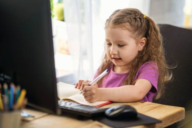 Küçük kız evde çalışmak için bir bilgisayar kullanıyor. Çocuk mutlu bir şekilde gülümser ve uzaktan bilgi alır. Dijital e-öğrenme konsepti, salgın sırasında, karantina ve kendini izole etme. Uzak e- öğrenme.