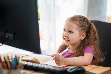 Küçük kız evde çalışmak için bir bilgisayar kullanıyor. Çocuk mutlu bir şekilde gülümser ve uzaktan bilgi alır. Dijital e-öğrenme konsepti, salgın sırasında, karantina ve kendini izole etme. Uzak e- öğrenme.