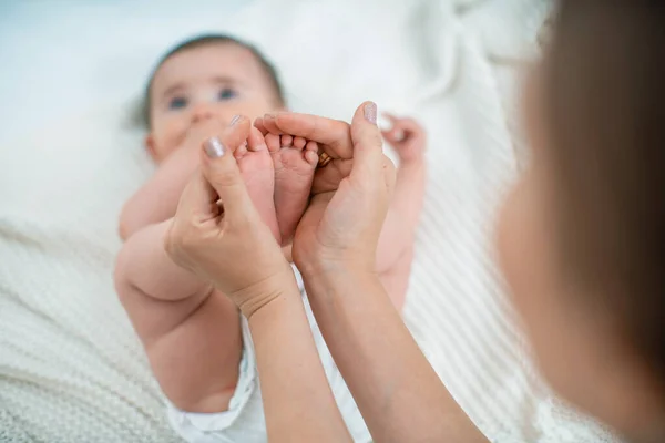 Close-up of children\'s foot massage on the bed. A mother massages the foot of a cute newborn baby\'s foot. Selective focus on the child\'s leg.