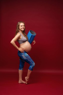 Spor elbiseli hamile bir kadın elinde bir spor ayakkabısı tutuyor. Müstakbel anne kırmızı arka planda gülümsüyor. Hamilelik süresince sağlıklı yaşam biçimi kavramı.