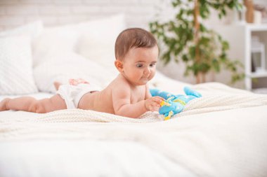 4 aylık tatlı tombul bebek, yumuşak örgü bir battaniyenin üzerine uzanmış ve kumaştan yapılmış bir oyuncağa bakıyor. Küçük bir çocuk emeklemeyi öğrenir. Boşluğun bir kopyası.