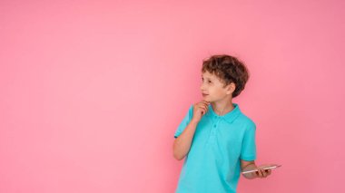 Dalgalı saçlı, Polo tişörtlü, akıllı telefonu elinde tutan ve pembe arka planda başka yere bakan düşünceli bir çocuk. Dijital teknolojiler, internet. Boşluğu kopyala