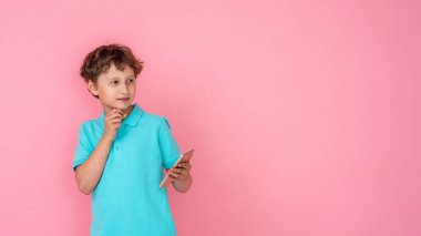 Dalgalı saçlı, Polo tişörtlü, akıllı telefonu elinde tutan ve pembe arka planda başka yere bakan düşünceli bir çocuk. Dijital teknolojiler, internet. Boşluğu kopyala