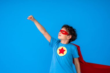 brave boy in a superhero costume, wearing a red Cape and mask, held out his hand as a sign of desire to win, isolated on a pink background. Cute kid playing superhero. The concept of power and justice clipart