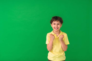 positive child exults with clenched fists, celebrates victory, wears a casual yellow t-shirt, and when successful, exclaims with joy. People and the concept of celebration, happy moment of life, luck clipart