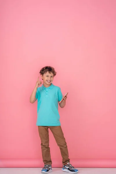 一个留着波浪般的头发 穿着Polo衫的笑脸男孩 手里拿着智能手机 在粉色的背景下站了起来 数字技术 互联网 复制空间 — 图库照片