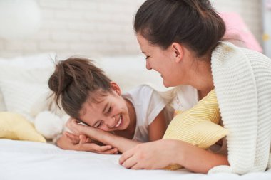 Sevgi dolu bir aile! Güzel beyaz anne ve kız kucaklaşır, eğlenir ve yatakta uzanıp eğlenirler. Bir kadın küçük, neşeli bir kızı gıdıklıyor ve neşeyle gülüyorlar..