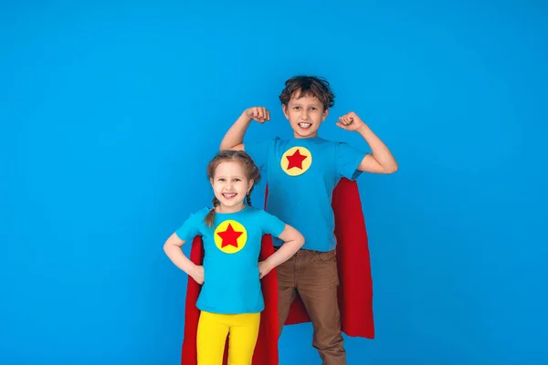 Funny little kids super hero power in red raincoats and mask. The concept of a superhero. Studio portrait over blue background. a team of heroes ready to fight. strong little children
