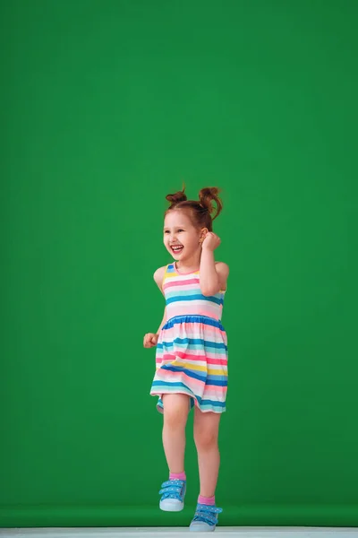 一个穿着五颜六色的条纹连衣裙跑着笑着的有趣滑稽的4岁女孩 工作室拍摄的绿色背景 幸福和无忧无虑的童年的概念 转过去看 — 图库照片