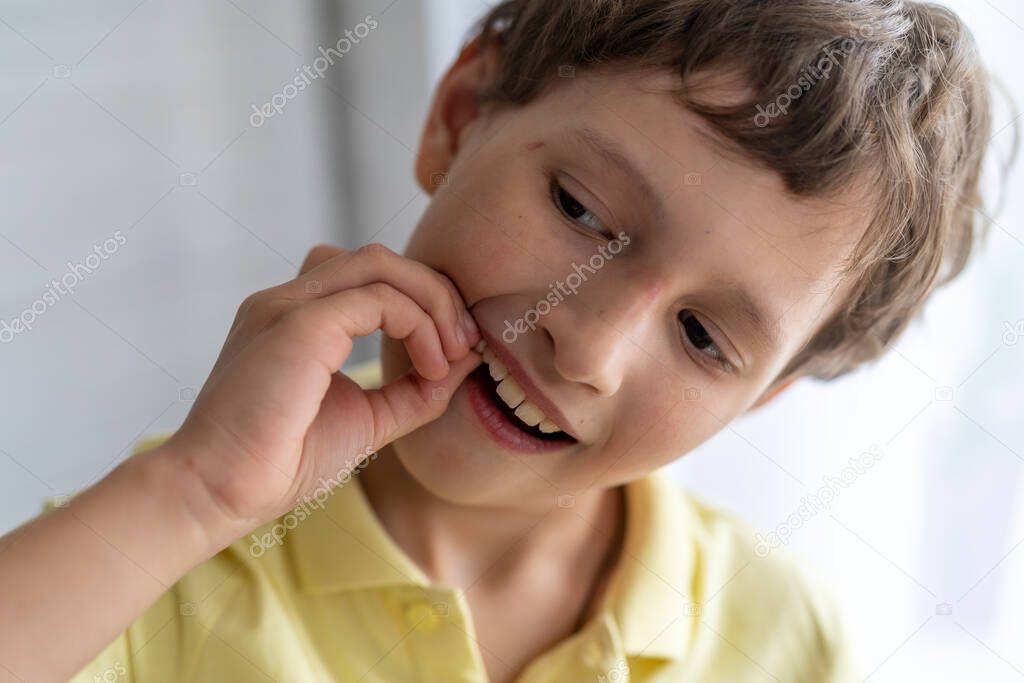 A brave little boy of 7 years old shakes his baby tooth. Change of teeth in children. Self-treatment at home.