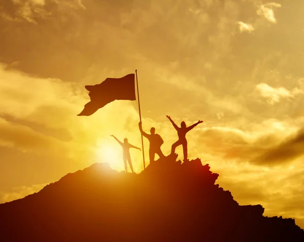 Alto sucesso, família três silhueta, pai de mãe e criança segurando bandeira da vitória no topo da montanha, mãos para cima . — Fotografia de Stock