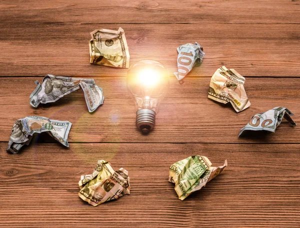 Eine Glühbirnen-Idee, umgeben von zerknüllten Dollars. Die Lampe fing durch die Idee Feuer. wie man Geld verdient oder spart, Geld, Beitrag. — Stockfoto