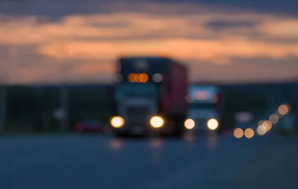 Blurred texture Traffic trucks with glowing lights on the highway after sunset. Lights of searchlights. Route, road, transport. Blue and orange bright sky at dusk.