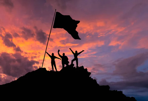 Conquistando la cima, siluetas de tres personas, con las manos en la cima de la montaña, con la bandera . — Foto de Stock