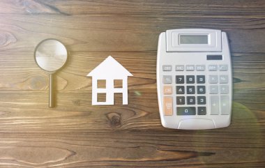 bir ev bir ipotek hesap makinesi ahşap arka plan üzerinde bir büyüteç ile hesaplanması