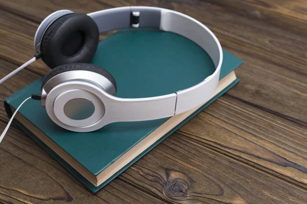 Audio book concept. Headphones and old book over wooden table.