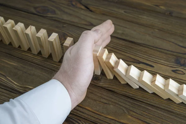 a male hand stopping the domino effect. retro style image executive and risk control concept. The business decision. closeup