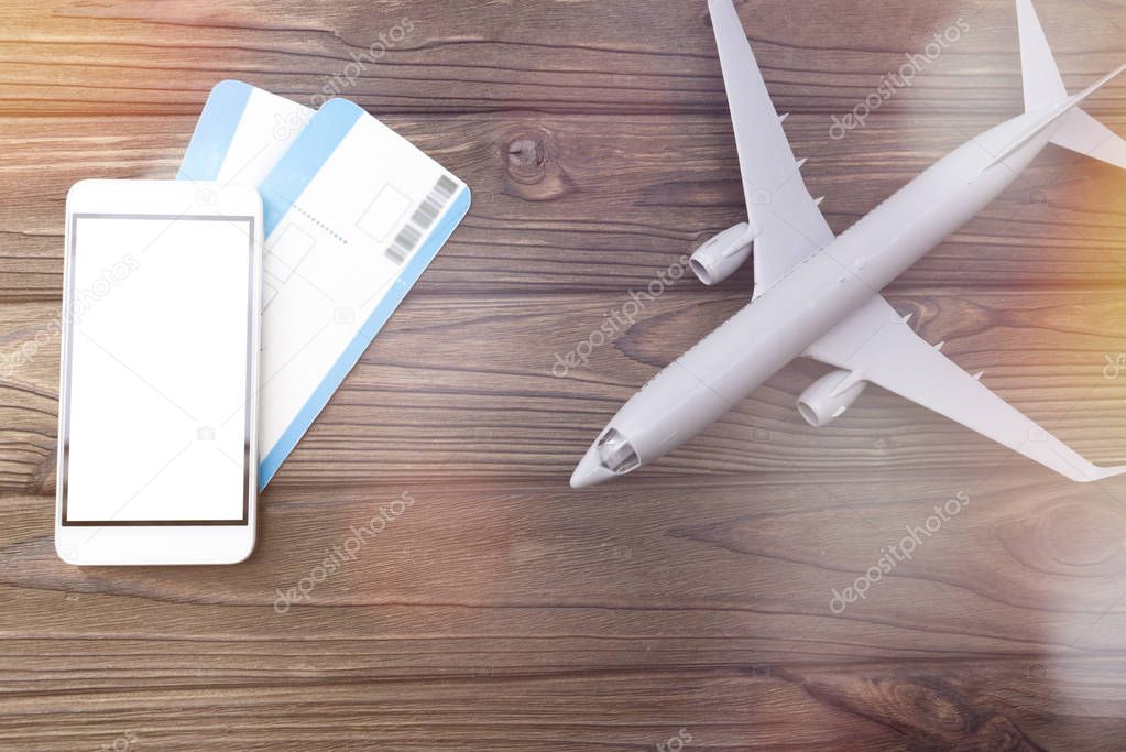 smartphone with white screen plane tickets, airplane on wooden background