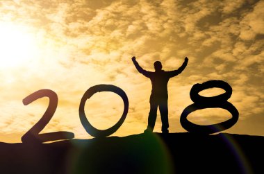 Bir adam silüeti bir dağın tepesinde ve güneş ışığı ile metin 2018 işaret mutlu yeni yıl takvim tatil kavramı üzerinde ellerini. Yeni yıl Noel