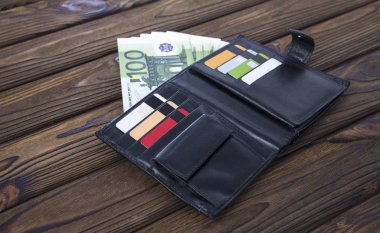 Ahşap masa arka plan üzerinde siyah Doğal deri cüzdan. Pahalı erkek cüzdan yakın çekim. Bir çanta yüz euro para ve plastik kart ile dolu. Fikir: iş, bankacılık