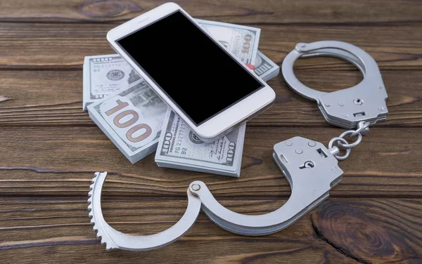 Konsept Telefon scammers. Smartphone, para, bir ağaç arka plan üzerinde kelepçe. Suç, dolandırıcılık, ceza, katılım.