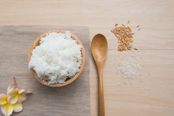 Arroz cocido en un tazón de madera y cuchara, arroz sobre un fondo de madera . — Foto de Stock