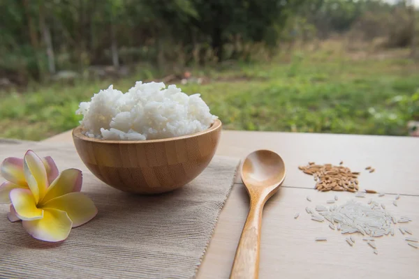 Arroz cocido en un tazón de madera y cuchara, arroz sobre un fondo de madera . — Foto de Stock