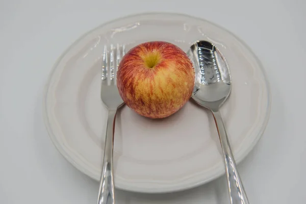 Czerwone jabłko na talerz i łyżka, widelec na białym tle — Zdjęcie stockowe