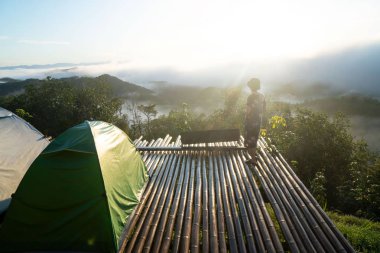 Genç bir kadın sabah sisinde mavi gökyüzü ve dağların muhteşem manzarası için ayakta duruyor. Başarı ve mutluluk konsepti için mutlu özgürlük.