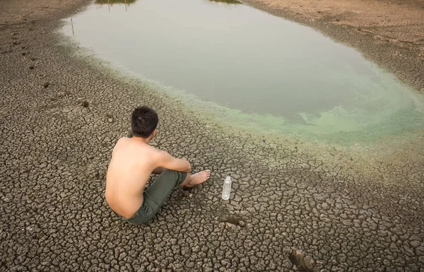Water crisis, man sit on cracked earth near drying water.